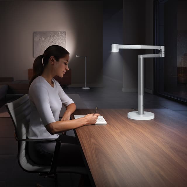 Kvinna som sitter vid ett skrivbord, med en Dyson lampa framför sig