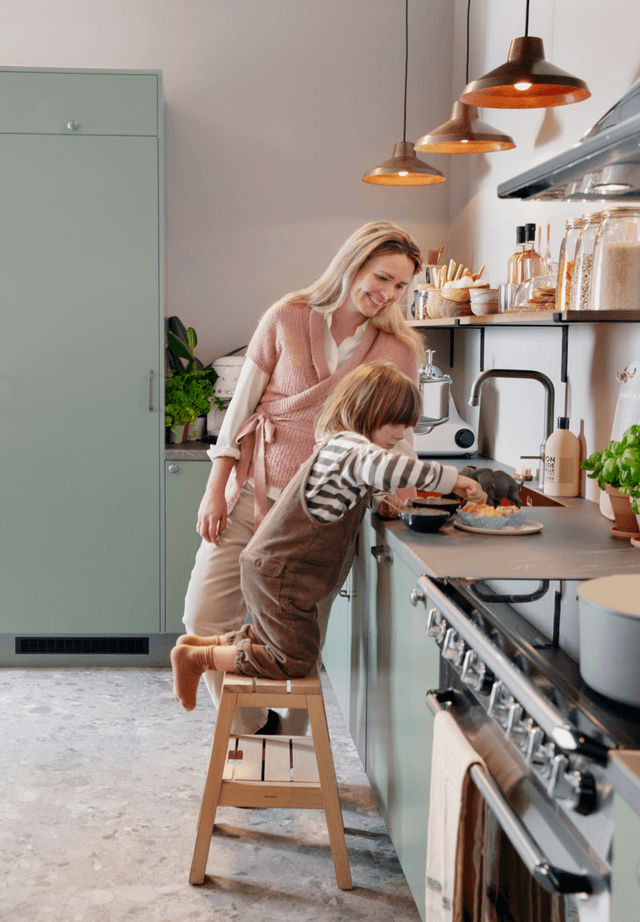Kvinne og barn på et grønt Trend Sage kjøkken med Smeg 90 cm bred komfyr