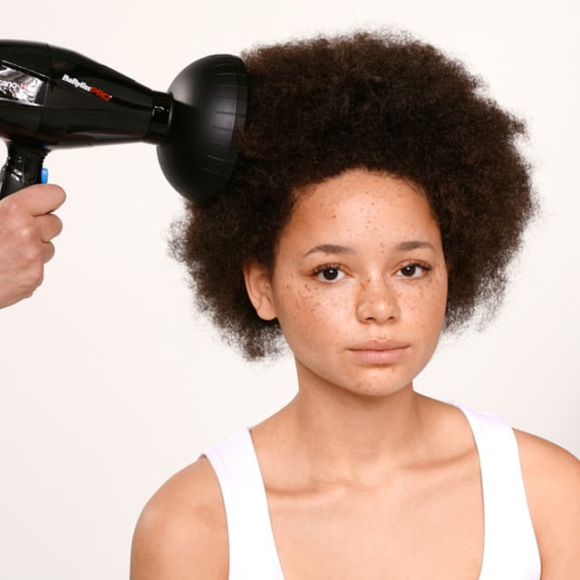 Kvine med mørk afro sopm får håret sitt fønet med en BaByLiss diffuser