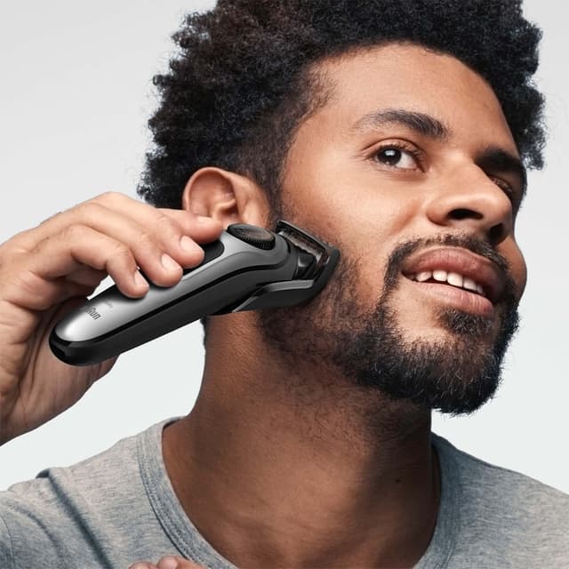 En mann trimmer skjegget med en Braun-trimmer