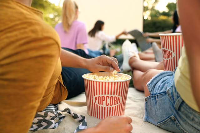 Par som äter popcorn och som tittar på en skärm utomhus med flera andra i en trädgård