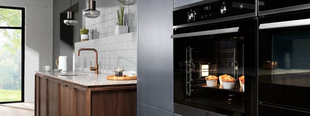 En dubbel Electrolux-ugn med muffins inuti med ett kök med bänkskiva och diskho med blandare i bakgunden