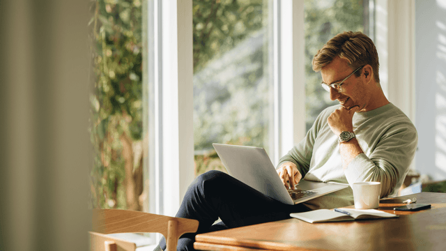 Hymyilevä mies istuu kannettavan edessä