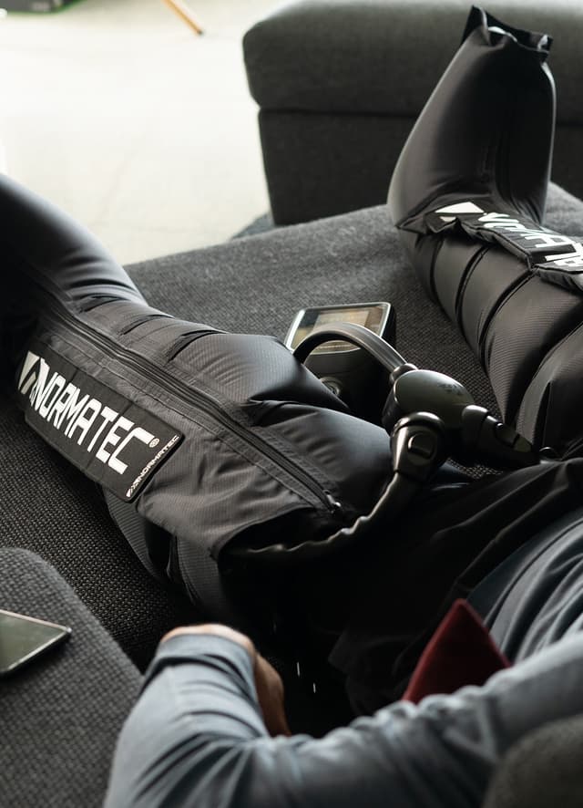 En kvinde ligger i en sofa ved hjælp af Hyperice Normatec Go benkompressionsmassager