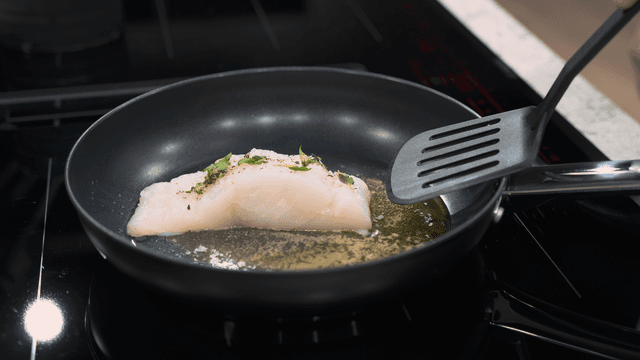 En person steker fisk i en stekpanna med en stekspade av plast