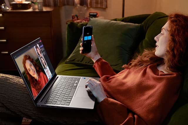Sohvalla istuva nainen käyttää Galaxy S24 Plus -älypuhelinta tietokoneeseen yhdistettynä kamerana
