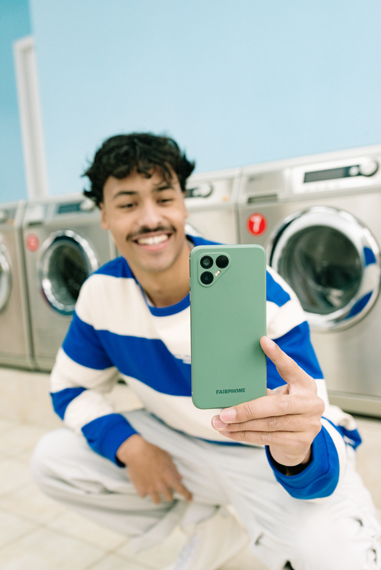 Fairphone 4-telefon i hånden på smilende mann som tar bilde i et vaskeri