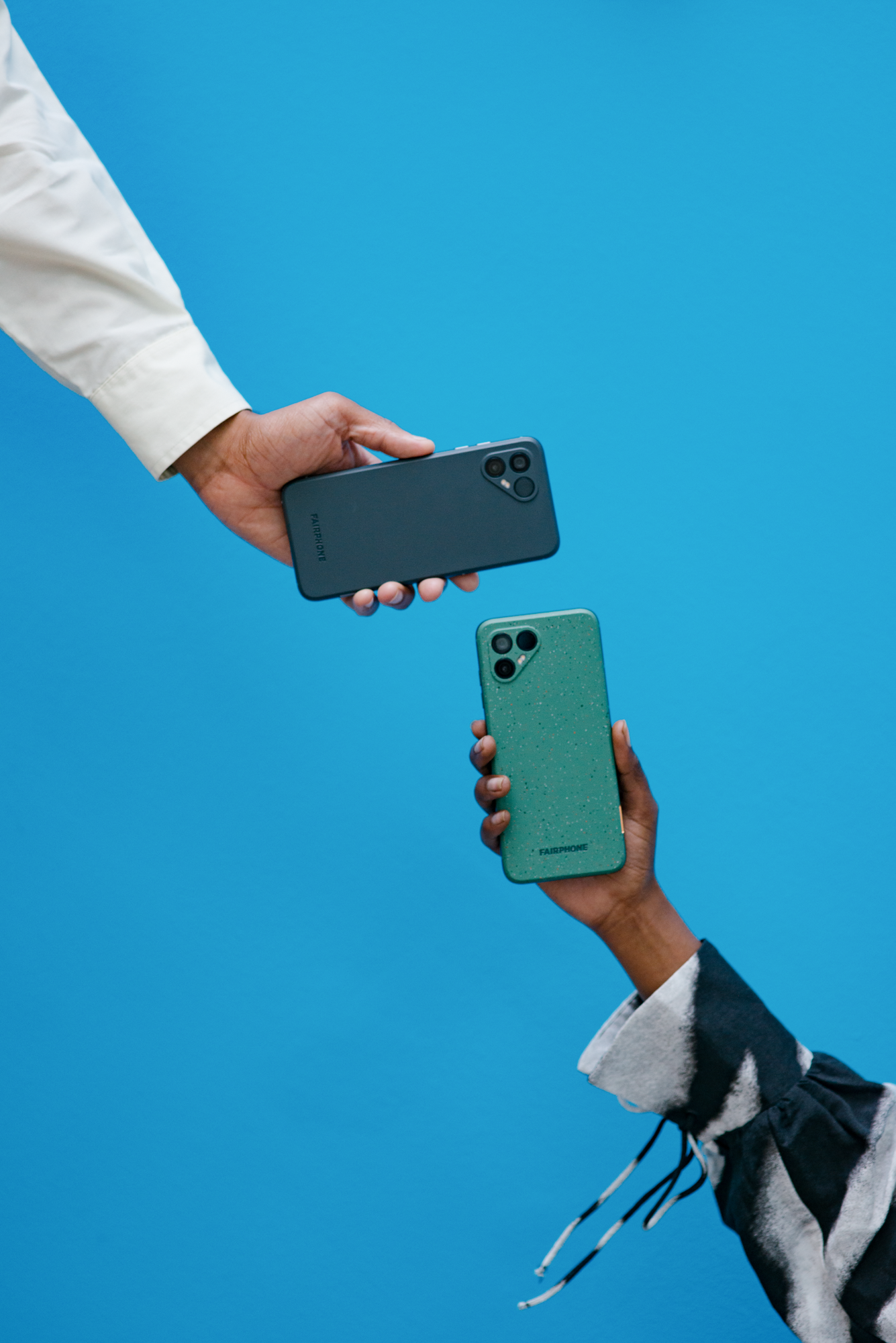 Fairphone 4 i grå og grønn farge holdt mot hverandre på blå bakgrunn