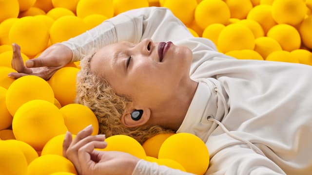 Jabra Elite høretelefoner og en kvinde der ligger blandt gule bolde