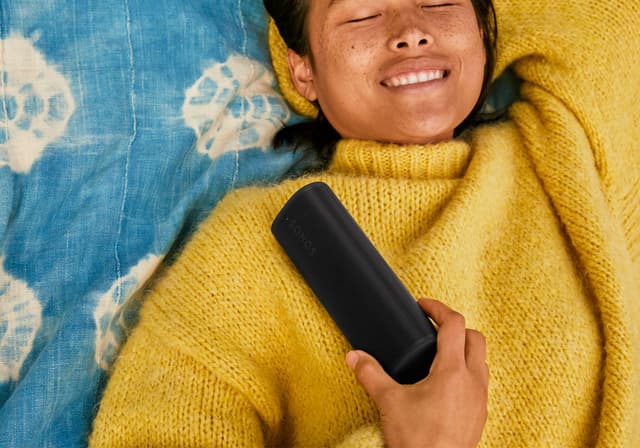 Nainen, jolla on keltainen neulepaita ja Roam 2 -kaiutin