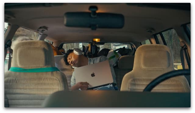 Ung studerende på bagsædet af en bil, der sover med MacBook Air på skødet og AirPods Max på