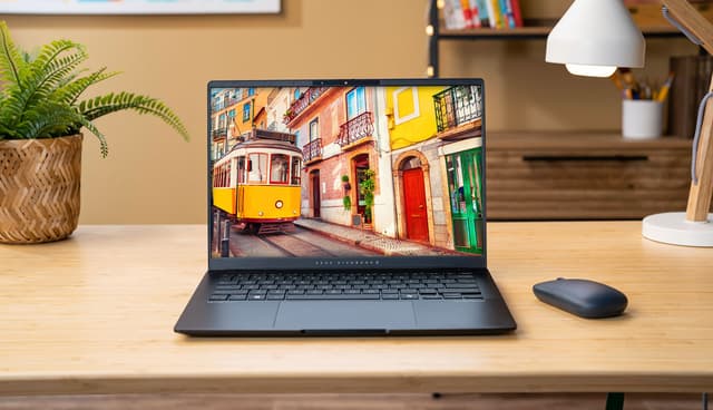 Asus Vivobook S 14 M5406 laptop on a table next to a mouse, lamp and a green plant