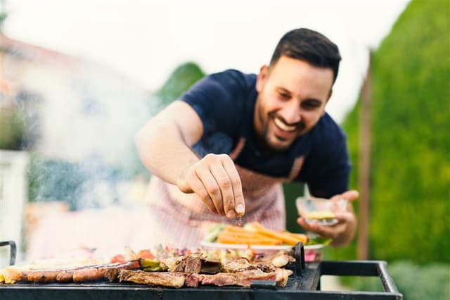 Mand læner sig ind over grill for at krydre den mad, han har lagt på