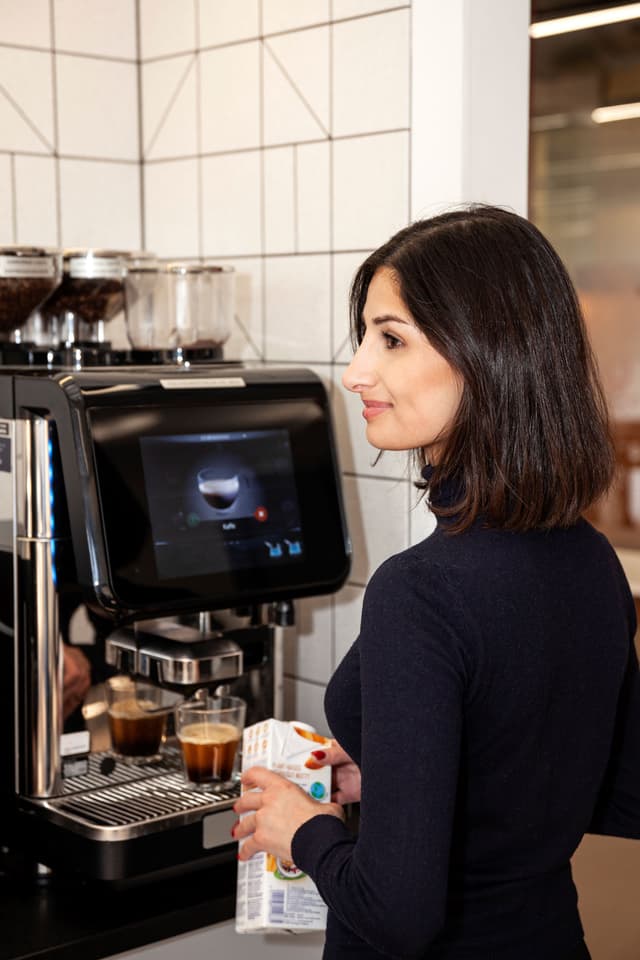 Kvinde står ved siden af ​​en kaffemaskine og venter på sin kaffe på et kontor