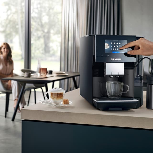 Siemens EQ700 kaffemaskin og en dame sitter i bakgrunnen og nyter kaffe