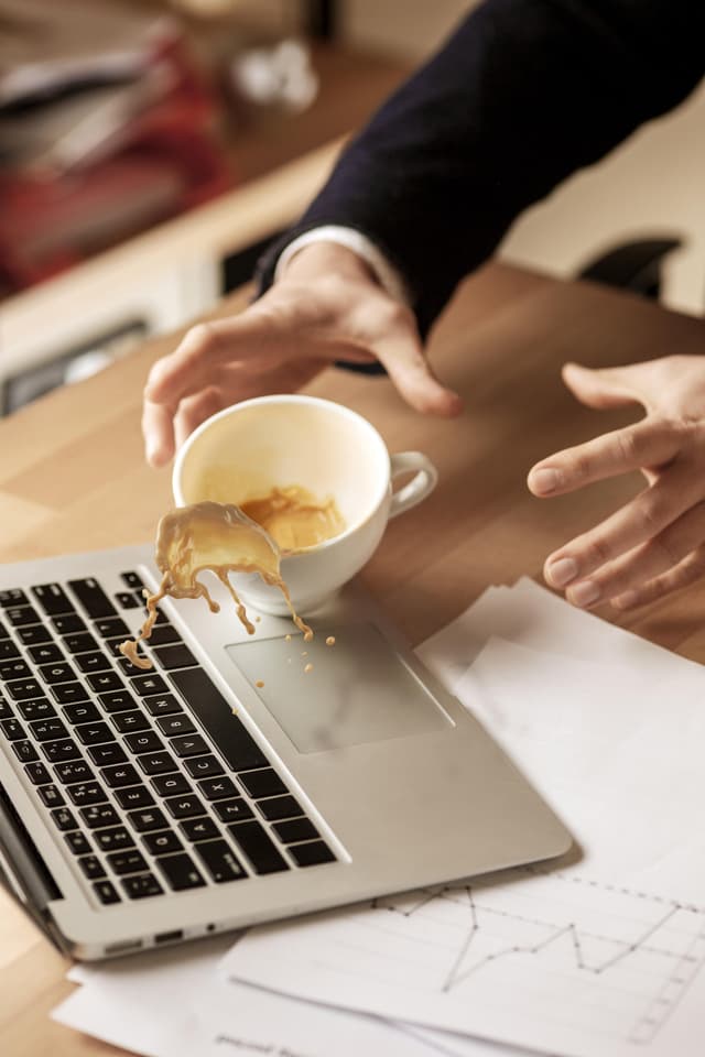 Coffee in white cup spilling on the laptop