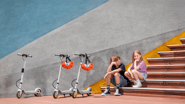 Girl and a boy sitting on a stairs next to electric scooters