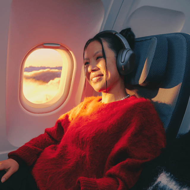 Girl sitting in a aeroplane and wearing JBL TOUR ONE M3 noice cancelling headphones in her head