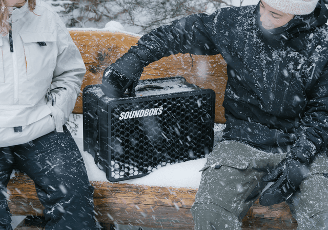 Soundboks Go - 2 personer som sitter på en snöig bänk och en bärbar Soundboks Go-högtalare mellan sig