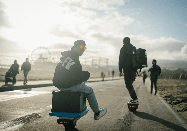Soundboks 4 – En mand med en transportabel Soundboks 4-højttaler på et elektrisk løbehjul