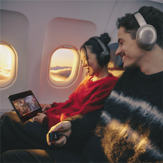 JBL TOUR ONE M3TX på hovedet af mand og på kvinde ombord på et fly