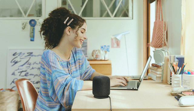 Black LinkBuds Speaker on a desk next to a girl who is working on her laptop