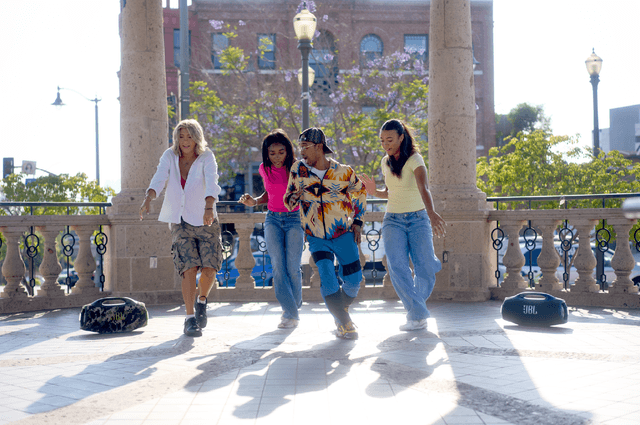 Neljä nuorta naista tanssivat kaupungilla, vieressä kaksi JBL Boombox 4 -kaiutinta