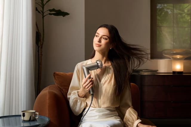 Kvinne tørker håret med stylingverktøy sittende i stue