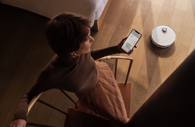 Kvinne fotografert ovenfra mens hun styrer Dreame X50 Ultra via Dreame Home-appen