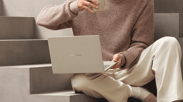 Mies istuu matalilla portailla juoden kahvia ja tehden töitä Zenbook A16 -kannettavalla