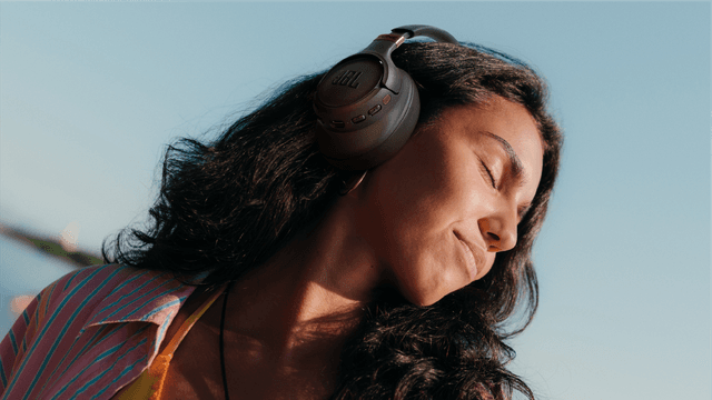 Smilende kvinne med lukkede øyne og JBL Tune 785-hodetelefoner på.