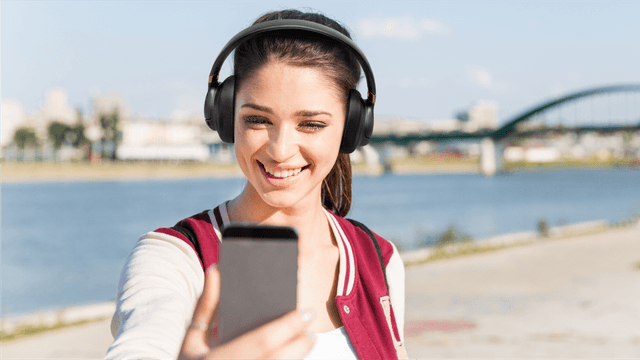 En kvinne i et videoanrop utendørs med JBL Tune 785- hodetelefoner på.