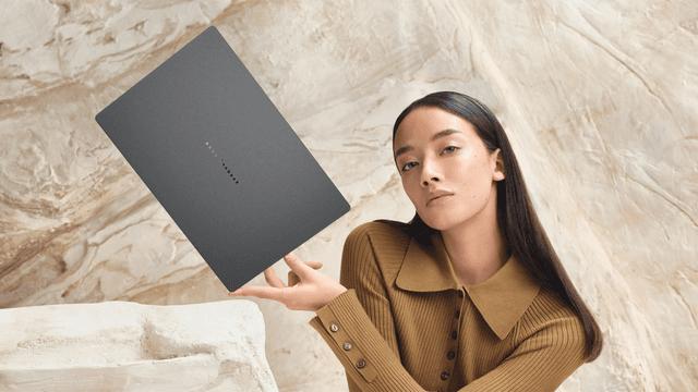 Kvinde holder en slank Zenbook A14‑laptop foran en stenvæg