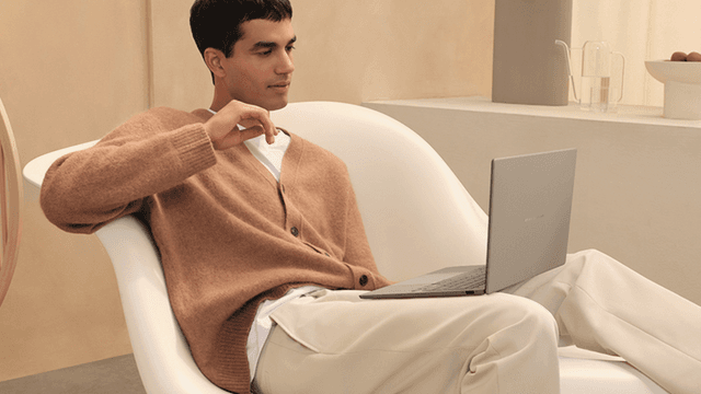 Mand slapper af i en hvid lænestol, mens han bruger en Zenbook A14‑laptop