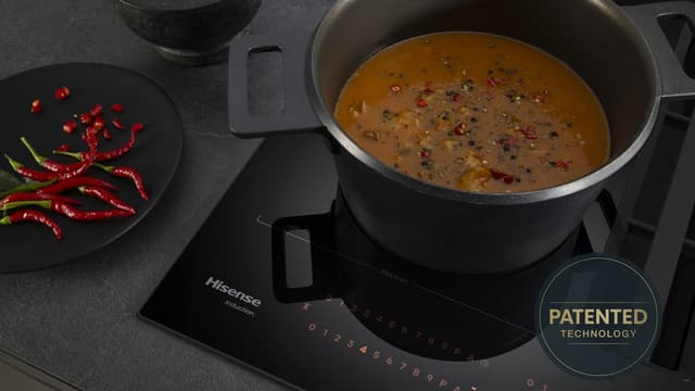 En gryterett koker på en Hisense-platetopp ved siden av en tallerken med rød chili.