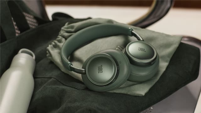 Grønne JBL 780 NC-hodetelefoner på en grønn tøypose på et sete ved siden av en vannflaske.