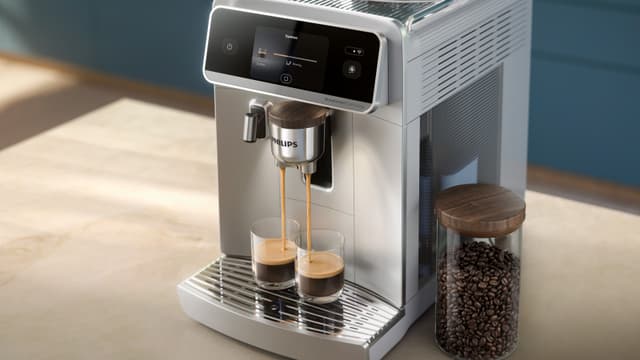 Philips 8000 Café Aromis kaffemaskine brygger kaffe i to kopper ved siden af en beholder med kaffebønner
