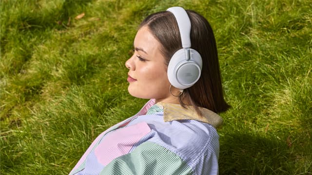 Kvinde sidder i græsset med hvide JBL Live 780 NC høretelefoner
