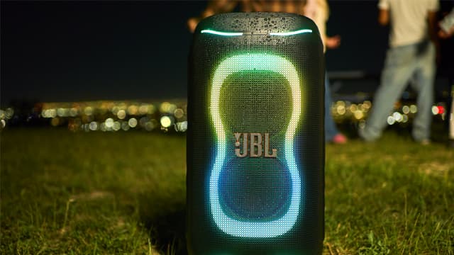 En JBL PartyBox 130 högtalare täckt i regndroppar på en gräsmatta.