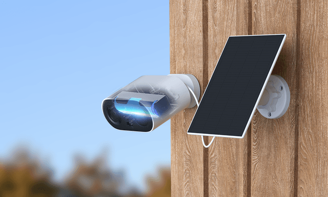 Et IMOU Cell Go Full Color-sikkerhetskamera ved siden av medfølgende solcellepanel på en yttervegg i tre.