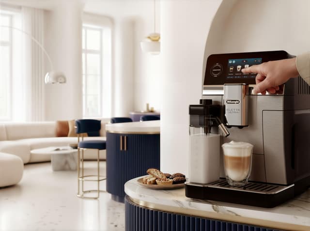 En DeLonghi Eletta Ultra-kaffemaskin på en marmorbenk med en nylaget cappuccino ved siden av en tallerken med kjeks.