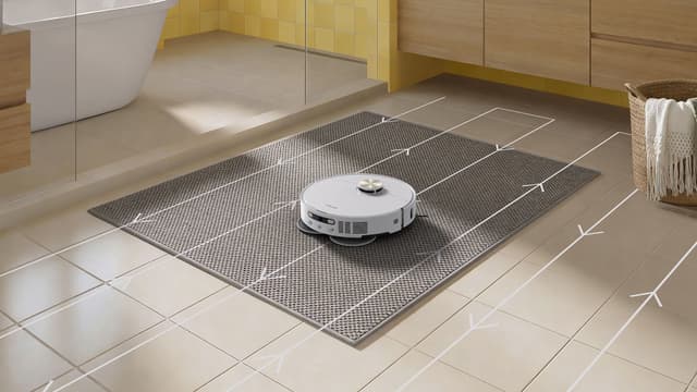 En Dreame L50 Ultra AE-robot rengjør et baderomsgulv ved siden av hvite illustrerende piler som viser rengjøringsmønsteret.