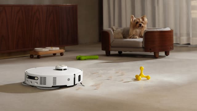 Dreame L50s Pro Ultra vasker et skittent gulv foran hundeseng med en hund i.