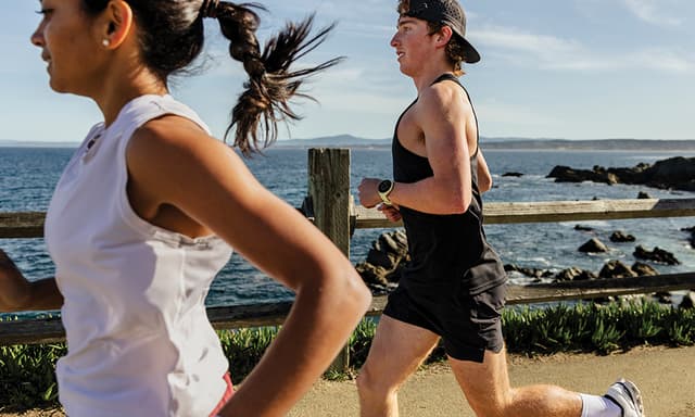 Mies ja nainen lenkkeilevät rantaviivaa pitkin Garmin Forerunner 70 & 170 -urheilukellot ranteissaan