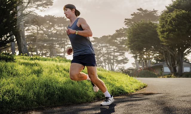 En mann som løper i en stille gate med en Garmin Forerunner-sportsklokke på armen.