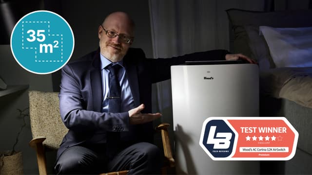 En man i kostym och glasögon sitter på en stol bredvid Woods Cortina bärbara AC och en markering som säger "Test winner"