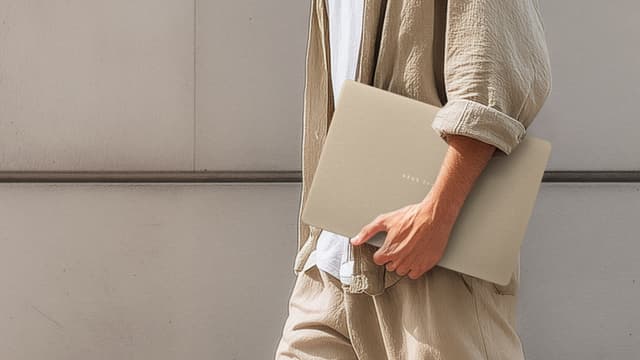 Henkilö kantaa kainalossaan beigeä ASUS Zenbook 14 UX3480 -kannettavaa