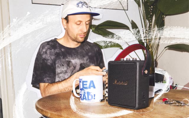 En mann sitter ved et kjøkkenbord med en Marshall Stockwell III-høyttaler mellom nøkler og en kaffekopp.