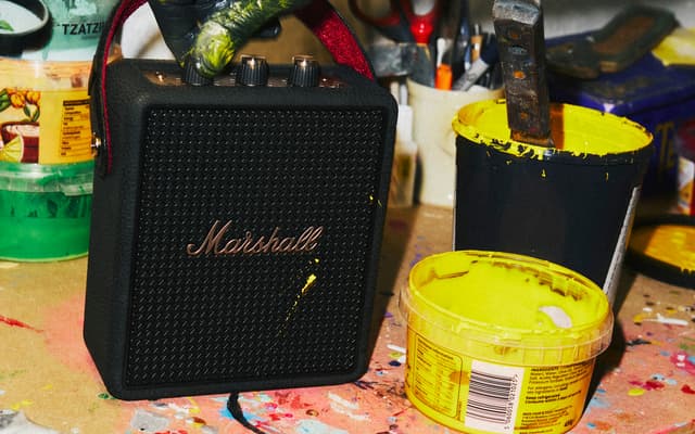 A black Marshall Stockwell III speaker on the ground next to pots of paint.