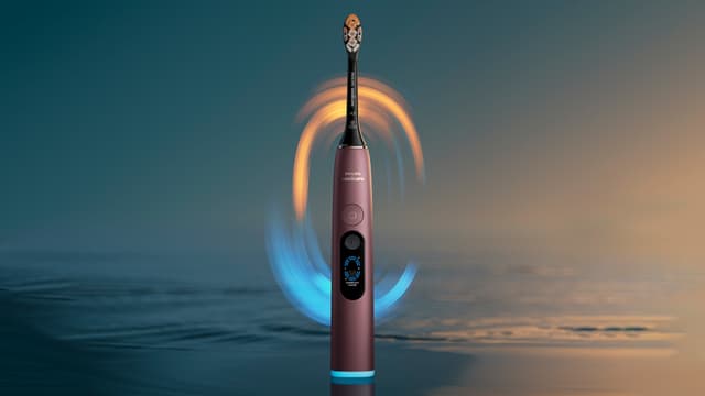 En burgunderlilla Philips Sonicare DiamondClean elektrisk tannbørste med hav og blått og gult lys i bakgrunnen.